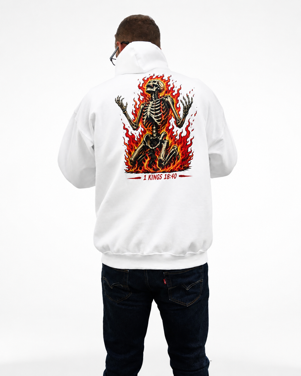 A man viewed from behind wearing a white pullover hoodie with a large graphic print on the back. The graphic features a skeleton surrounded by red and orange flames, with the text '1 KINGS 18:40' printed below in red.