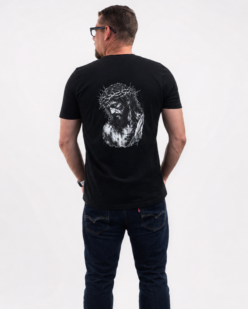 A man viewed from behind wearing a black t-shirt with a large white graphic of Jesus on the back, paired with dark blue jeans, against a plain white background.
